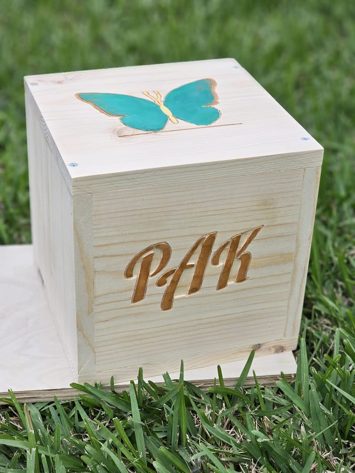 A pine piggy bank carved with the initials P A K and a turquoise butterfly on the lid